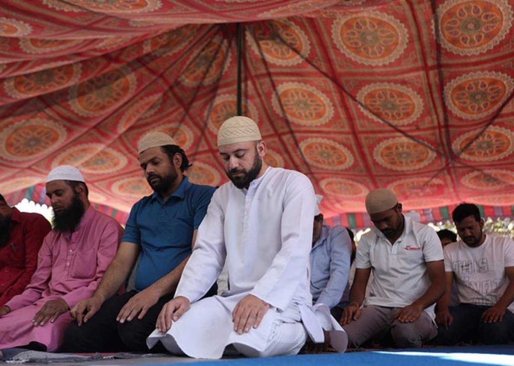 مجموعة من الرجال يؤدون الصلاة في خيمة مزينة بنمط تقليدي، حيث يركزون على الصلاة مع تباين في الألوان والملابس.